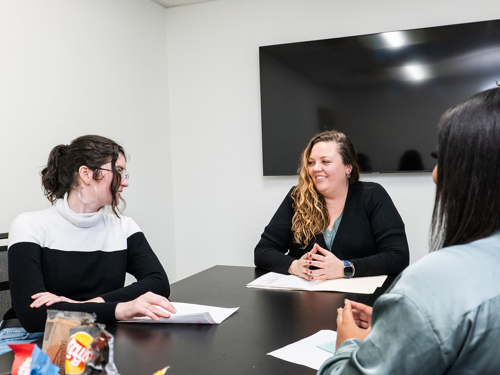 Three women sitting around a conference table with papers in front of them.