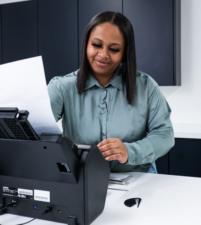 A woman in a green shirt puts a document into a scanner.